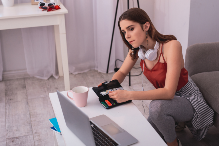 Teenager holding wallet looking at laptop computer