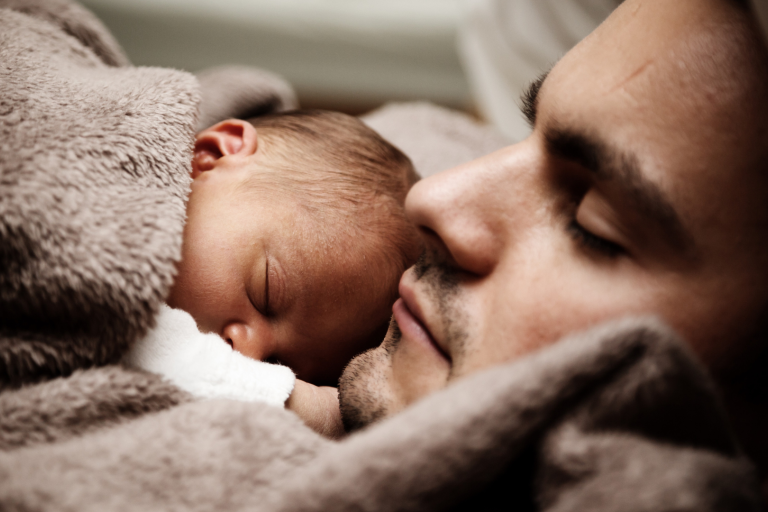 baby lying on dads chest under a blanket