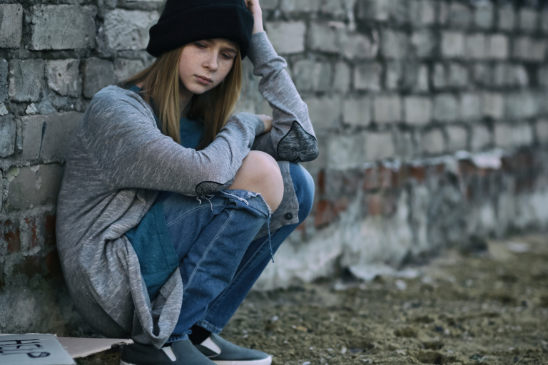 Teenage girl knelt down with back up against brick wall